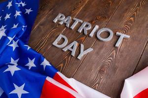 as palavras patriot day colocado com letras de metal prateado na superfície da placa de madeira com bandeira dos eua amassada foto