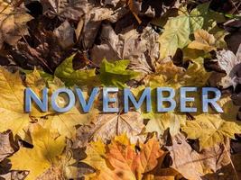 a palavra novembro colocada com letras de metal sobre folhas caídas de outono amarelo - closeup com foco seletivo foto