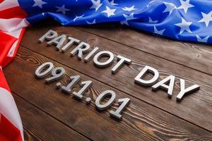 as palavras patriot day colocado com letras de metal prateado na superfície da placa de madeira com bandeira dos eua amassada foto