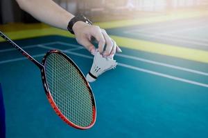 jogador de badminton segura raquete e peteca de creme branco na frente da rede antes de servir para o outro lado da quadra. foto