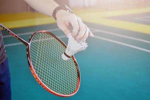 jogador de badminton segura raquete e peteca de creme branco na frente da rede antes de servir para o outro lado da quadra. foto