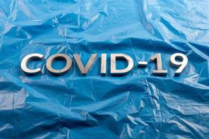 a palavra covid-19 colocada com letras de alumínio em fundo de filme plástico azul amassado em composição plana leiga foto