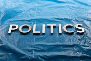 a palavra política colocada com letras de alumínio prateadas sobre fundo de filme azul plástico amassado - no centro da imagem foto