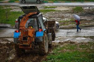 velho trator em dia chuvoso fazendo trabalho de sujeira no gramado perto da estrada foto