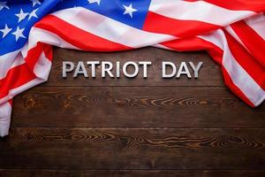 as palavras patriot day colocado com letras de metal prateado na superfície da placa de madeira com bandeira dos eua amassada foto