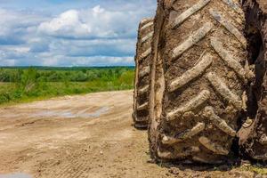 rodas duplas sujas de trator agrícola na estrada de terra no dia ensolarado de verão com campo verde ao fundo foto