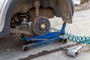 carro sem roda levantado com macaco hidráulico e chave de impacto pneumática em uma oficina de automóveis ao ar livre. procedimento de troca de pneus da estação. foto