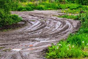zig-zag de estrada de lama de barro sujo com poças e marcas de pneus - closeup com foco seletivo foto