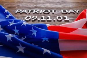 as palavras patriot day colocado com letras de metal prateado na superfície da placa de madeira com bandeira dos eua amassada foto