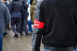 homem civil com braçadeira vermelha assinou o esquadrão do povo em russo - de pé na multidão, close-up com foco seletivo foto