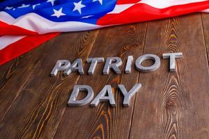 as palavras patriot day colocado com letras de metal prateado na superfície da placa de madeira com bandeira dos eua amassada foto