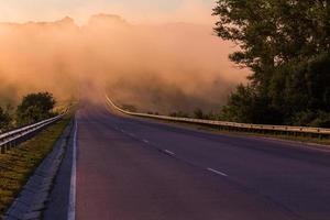 denso nevoeiro matinal em wold na estrada de verão perto do rio com guarda-corpos foto