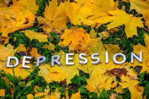 a palavra depressão colocada com letras grossas de alumínio no chão com folhas de bordo, grama verde e copyspace. foto