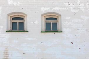 duas janelas na parede medieval de tijolos grossos sob camada desgastada de gesso branco foto