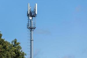 torre de telecomunicações de tubo cinza com topo de árvore verde no céu azul com fundo de nuvens foto