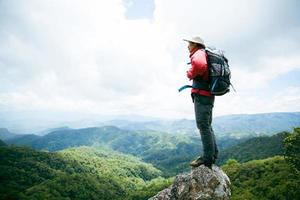 jovem caminhadas masculinas no topo da rocha, mochila homem olhando para o belo vale da montanha à luz do sol no verão, paisagem com esporte homem, altas colinas, floresta, céu. viagem e Turismo. foto