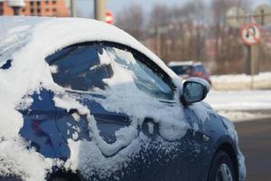 carro azul coberto de neve andando na rua de dia de inverno foto