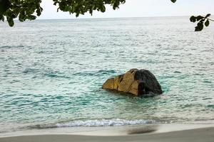 uma grande pedra que fica na praia dividindo as ondas foto