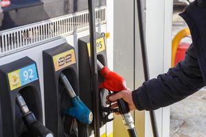 mão de velho tomando bico de combustível vermelho 95 gasolina do posto de gasolina à luz do dia. foto