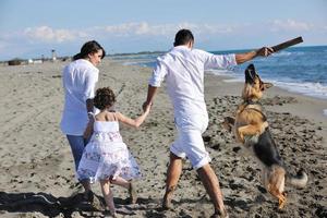 família feliz brincando com cachorro na praia foto