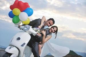 casal recém casado na praia anda de scooter branca foto