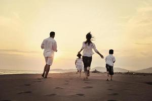 família jovem feliz se diverte na praia ao pôr do sol foto