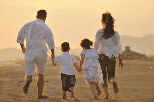 família jovem feliz se diverte na praia ao pôr do sol foto