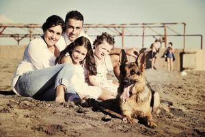 família feliz brincando com cachorro na praia foto