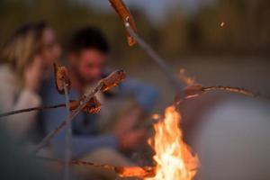 grupo de jovens amigos sentados à beira do fogo na praia foto