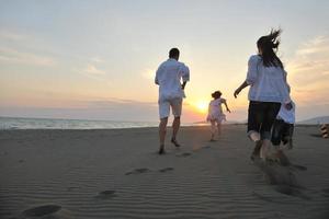 família jovem feliz se diverte na praia ao pôr do sol foto