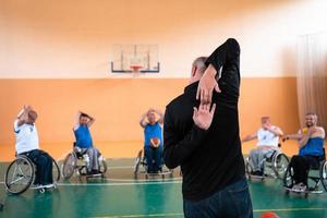 o selecionador do time de basquete com deficiência fica na frente dos jogadores e mostra os exercícios de alongamento antes do início do treinamento foto