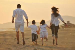 família jovem feliz se diverte na praia ao pôr do sol foto