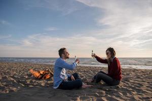 jovem casal sentado na praia ao lado da fogueira bebendo cerveja foto