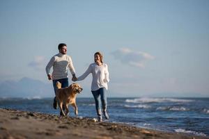 casal com cachorro se divertindo na praia no dia de autmun foto