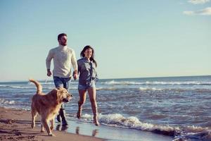 casal com cachorro se divertindo na praia no dia de autmun foto