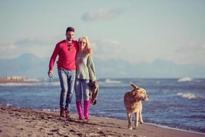 casal com cachorro se divertindo na praia no dia de autmun foto