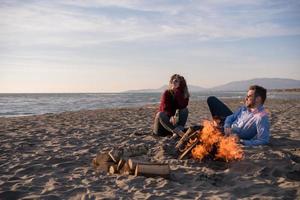 jovem casal sentado na praia ao lado da fogueira bebendo cerveja foto
