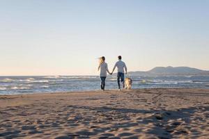 casal com cachorro se divertindo na praia no dia de autmun foto