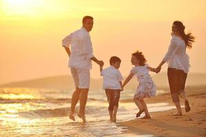 família jovem feliz se diverte na praia ao pôr do sol foto