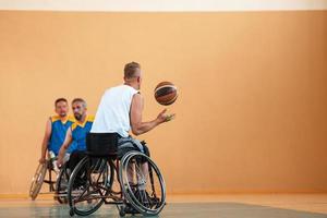 Veteranos de guerra com deficiência equipes de basquete de raça mista e idade em cadeiras de rodas jogando uma partida de treinamento em um ginásio de esportes. conceito de reabilitação e inclusão de pessoas com deficiência foto