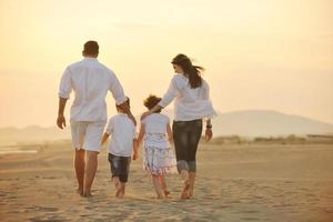 família jovem feliz se diverte na praia ao pôr do sol foto