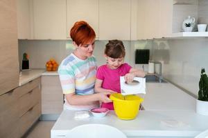 ajudante de garotinha engraçada brincando com massa nas mãos aprendendo a amassar ajuda a mãe adulta na cozinha, a filha do bebê fofo feliz e a mãe dos pais se divertem cozinhando biscoitos. foto