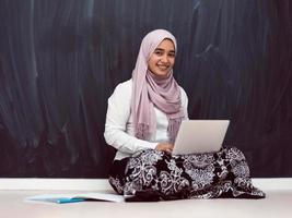 adolescente árabe com hijab sentado no chão da casa e assistindo aulas online durante a pandemia de coronavírus. foco seletivo foto