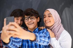 grupo de adolescentes árabes tirando foto de selfie no telefone inteligente com lousa preta no fundo. foco seletivo