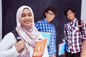 adolescentes árabes, retrato de grupo de estudantes contra lousa preta usando mochila e livros na escola. foto