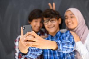 grupo de adolescentes árabes tirando foto de selfie no telefone inteligente com lousa preta no fundo. foco seletivo