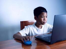 feche o menino fica olhando para o laptop e sua mão está segurando o mouse. conceito educacional, pesquisa de informações educacionais, espaço de cópia foto