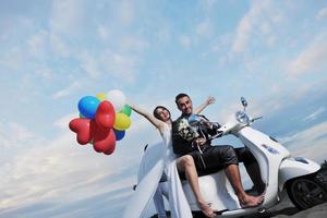 casal recém casado na praia anda de scooter branca foto