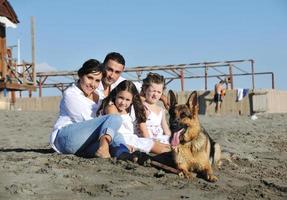 família feliz brincando com cachorro na praia foto