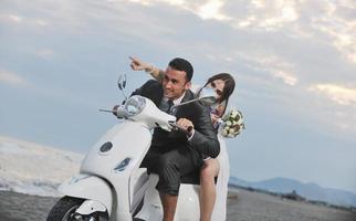 casal recém casado na praia anda de scooter branca foto